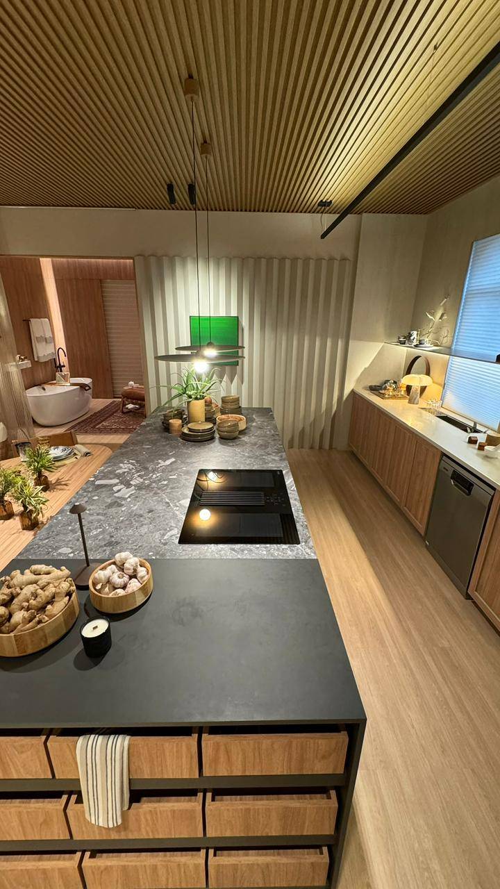 Cozinha com ilha em porcelanato claro e pendentes metálicos.